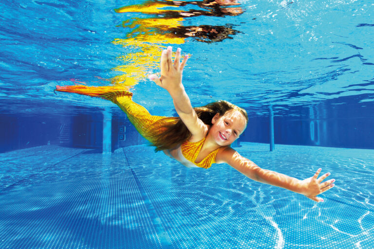 Mädchen als Meerjungfrau schwimmt im Schwimmbecken